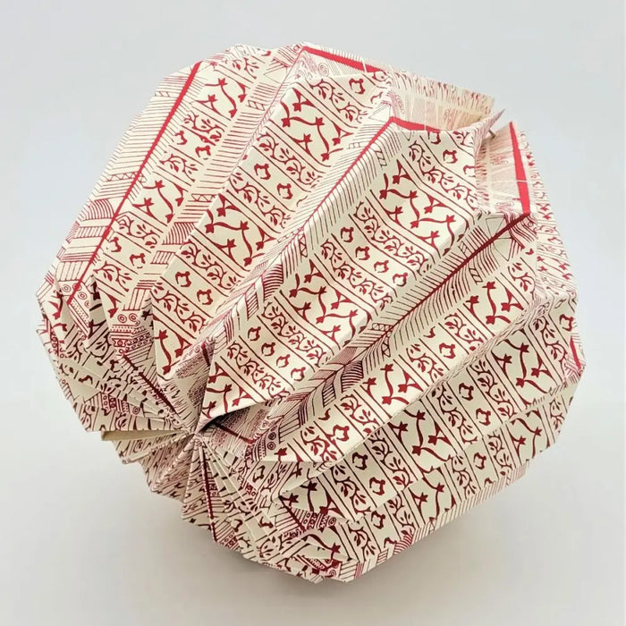 A cream-colored paper short pendant origami light shade with red geometric tribal-inspired patterns folded complexly