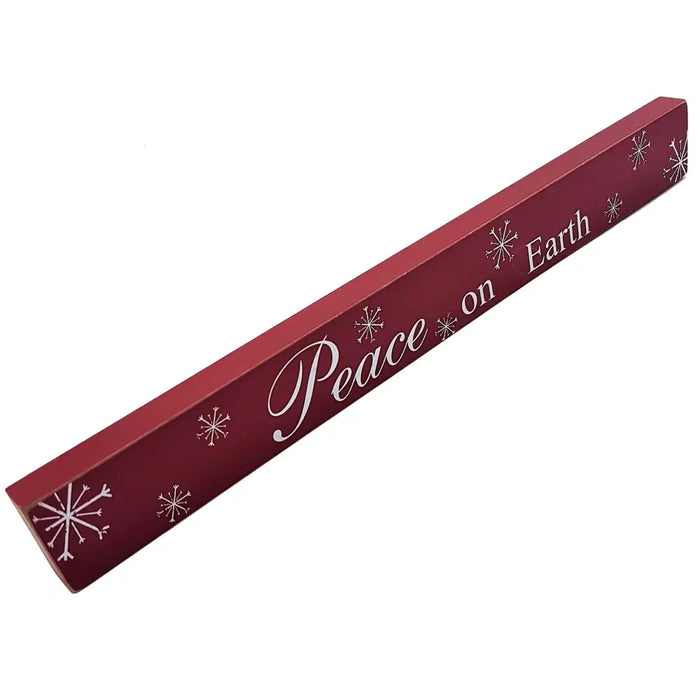 A maroon free-standing wooden plaque with white cursive peace on earth lettering and small snowflake designs