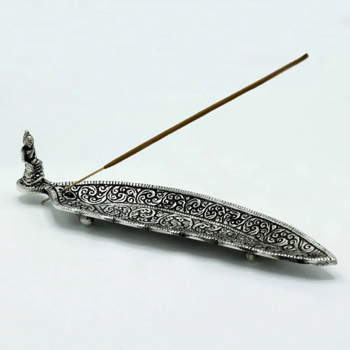 Polished aluminium incense holder long shaped with silver intricate swirling patterns and small buddha figurine at one end