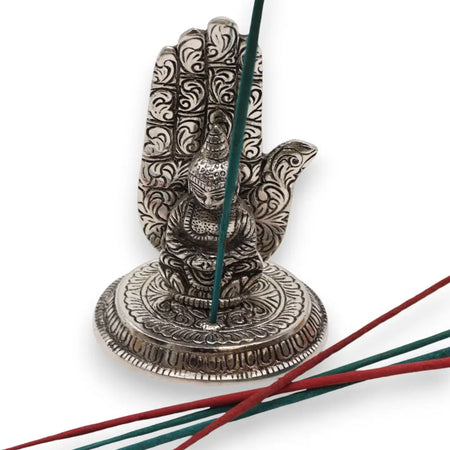 Silver polished aluminium incense holder shaped like a hand with floral engravings and a seated buddha figure in the center