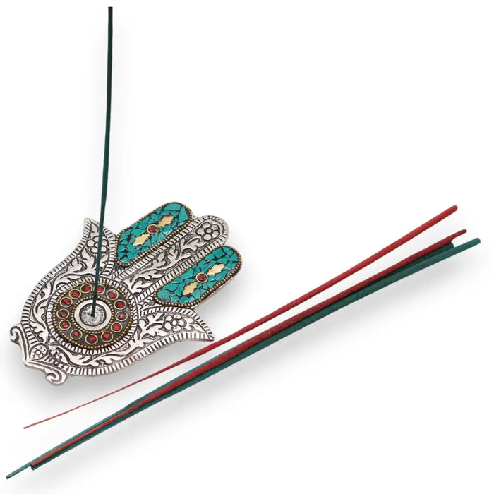 Polished aluminium incense holder shaped like a small silver hamsa with turquoise and red inlays holding a green stick