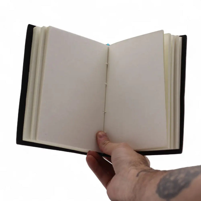 Black leather notebook with printed leather cover and wire binding showing blank white pages in a 7 by 5 size