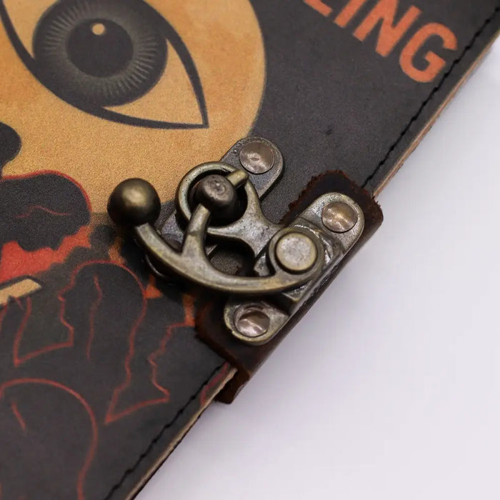 Antique brass anchor clasp on a dark leather notebook with printed eye illustration on the leather cover