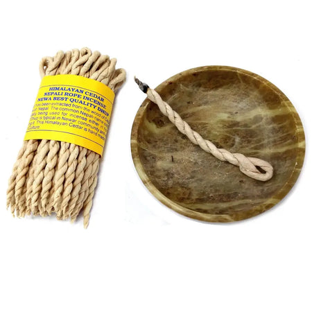 A bundle of beige himalayan cedar incense ropes with a yellow label and a twisted stick in a green marble ash bowl
