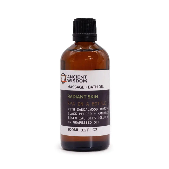 A brown glass bottle with black cap and white label of ancient wisdom radiant skin massage oil with essential oils