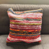 A vibrant rag rug cushion cover in aqua blues made from woven colorful fabric strips in a patchwork pattern
