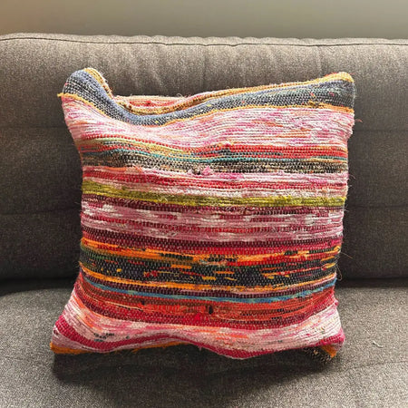 A vibrant rag rug cushion cover in aqua blues made from woven colorful fabric strips in a patchwork pattern