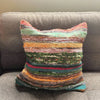 A handwoven rag rug cushion cover with charcoal greys and colorful stripes in earthy tones and vibrant hues
