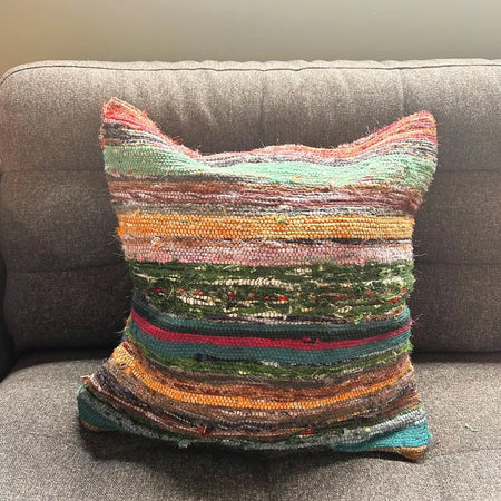 A handwoven rag rug cushion cover with charcoal greys and colorful stripes in earthy tones and vibrant hues