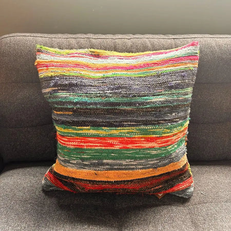 A multicolored rag rug cushion with horizontal stripes in natural greens and warm tones made from indian rag rugs