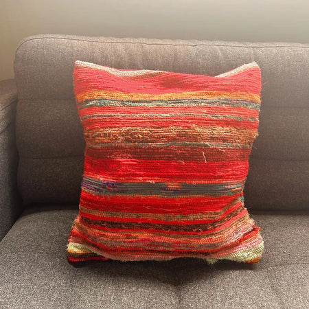 Vibrant red and orange striped rag rug cushion cover with rustic textured fabric in rich reds color scheme