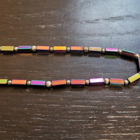 A rainbow hematite peninsular beaded necklace with iridescent rectangular and spherical magnetic beads in a gradient pattern