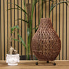 A dark brown rattan table lamp with a teardrop shape made of natural rattan and black spherical feet with plug fitting
