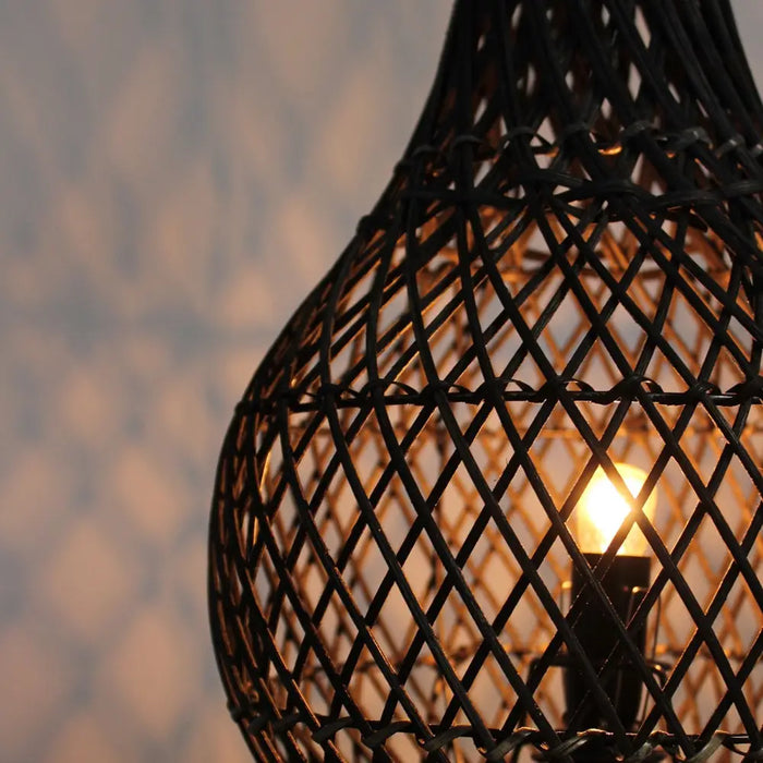 Black woven rattan table lamp with natural rattan shade casting delicate shadows and a warm glowing bulb inside