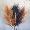A bundle of dried rayung grass with coral orange and deep purple feathery plumes tied at the base in a set of 3