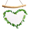 Green heart wind chime made of recycled glass hanging from natural driftwood branch outdoors