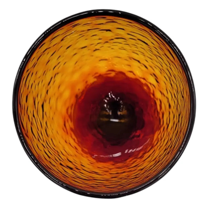 A hand-blown recycled glass wine glass in berry red with amber swirls and a textured woven surface