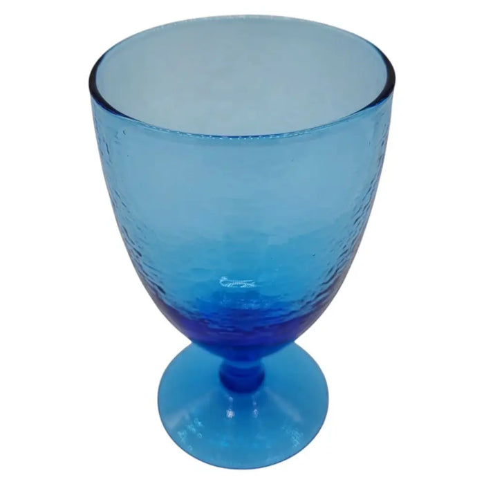A recycled glass wine glass in ice blue with a hammered texture and gradient finish from light to dark blue