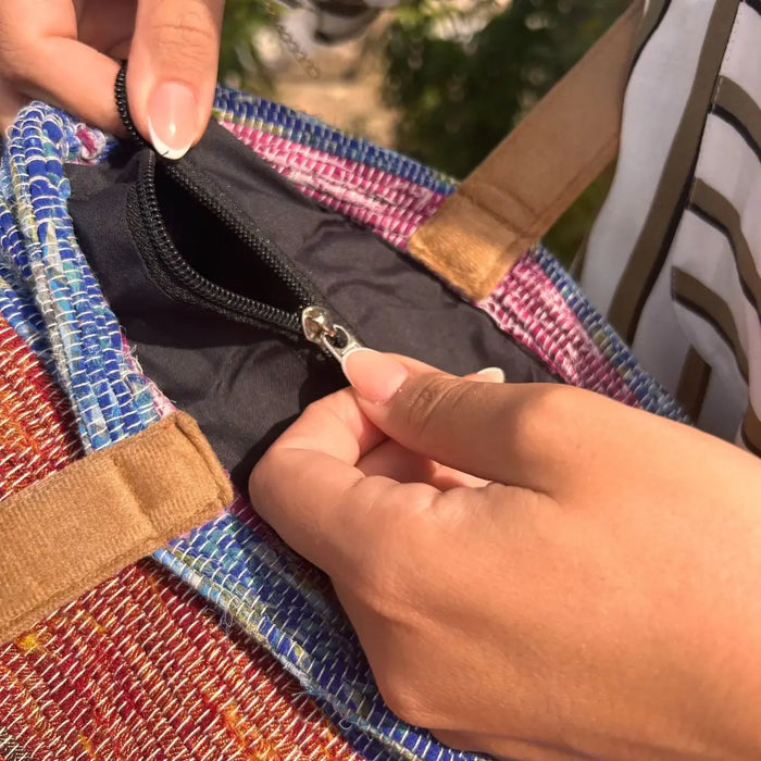 A colorful recycled rugs tote bag with black zipper and tan handles for carrying everyday essentials