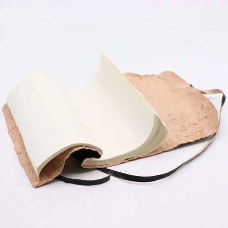 A rolled leather travel notebook with off-white textured paper bound in rustic brown leather and black ribbon straps
