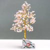 A rose quartz gemstone tree with delicate pink crystals and twisted gold wire on a painted stone base