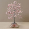 A rose quartz gemstone tree ornament with pink crystals and twisted silver wire on a crushed crystal acrylic base