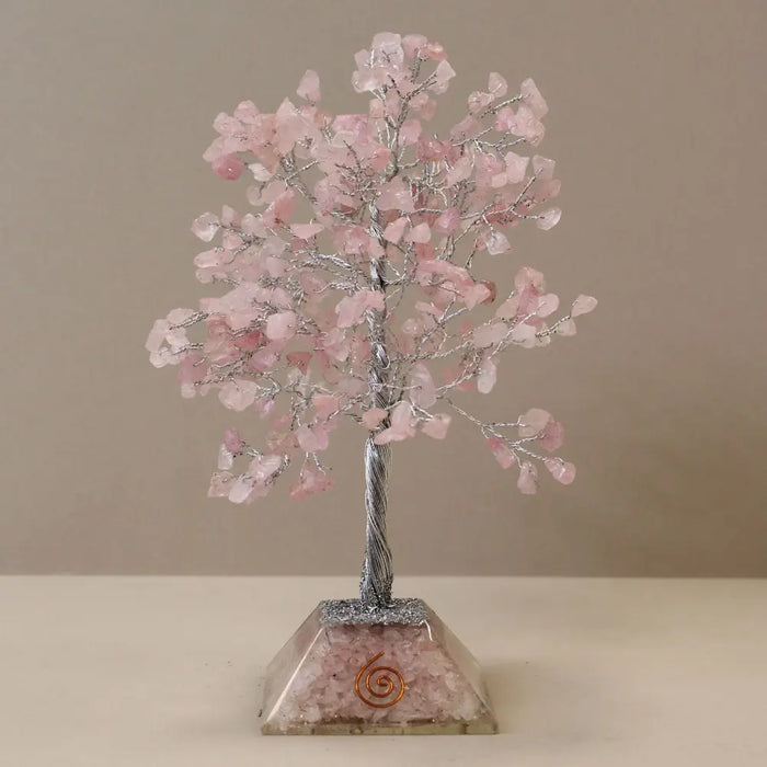 A rose quartz gemstone tree ornament with pink crystals and twisted silver wire on a crushed crystal acrylic base