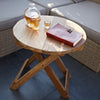 Clear glass skull-shaped decanter with amber liquid on round folding coffee table made of teak wood and recycled wood