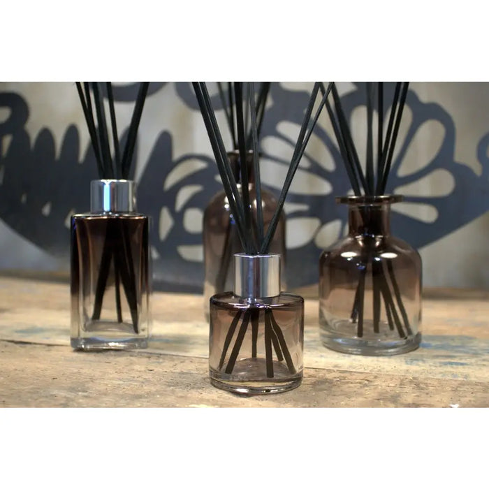 Three amber round reed diffuser bottles with screw cap and black bamboo reeds in a simple setup