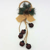 A rustic holiday wall hanging with dark brown jingle bells, faux pine, red berries, pinecones, and burlap ribbon