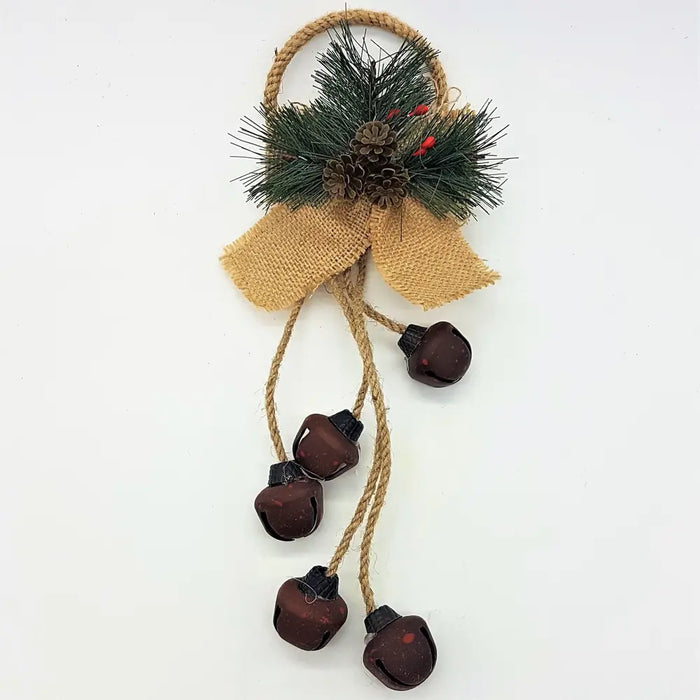 A rustic holiday wall hanging with dark brown jingle bells, faux pine, red berries, pinecones, and burlap ribbon