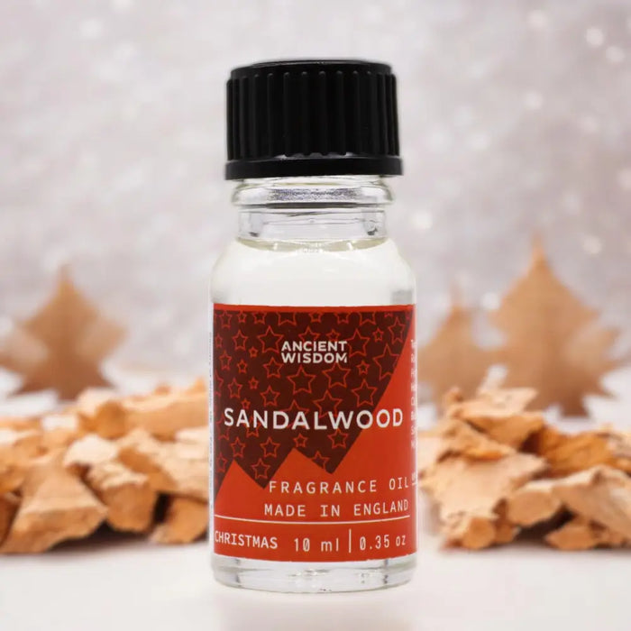 A clear glass bottle of sandalwood christmas fragrance oil with black cap red star label and allergen declarations