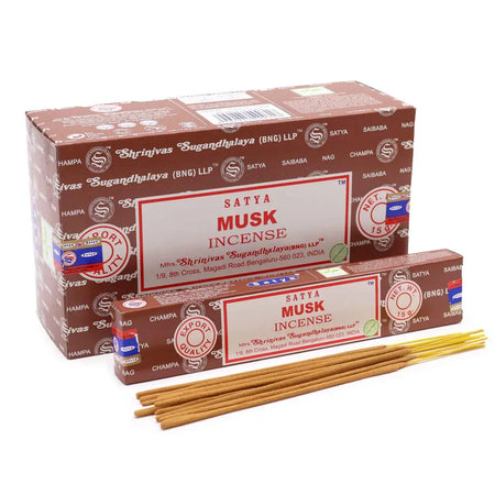 Brown cardboard box of satya incense sticks musk with white label red text next to loose golden brown incense sticks