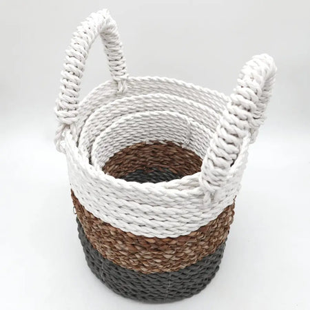 A set of three seagrass baskets in grey natural and white with striped pattern and thick rope handles