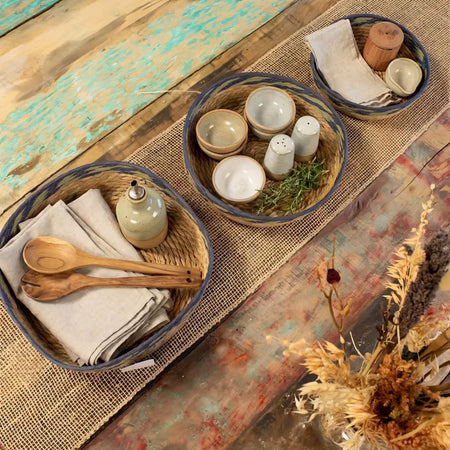 Handwoven tray basket set of 3 with blue-stained rim holding beige linen napkins and wooden utensils