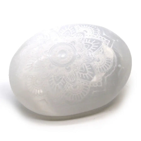 A translucent white selenite palm stone with an intricately engraved mandala design on its surface