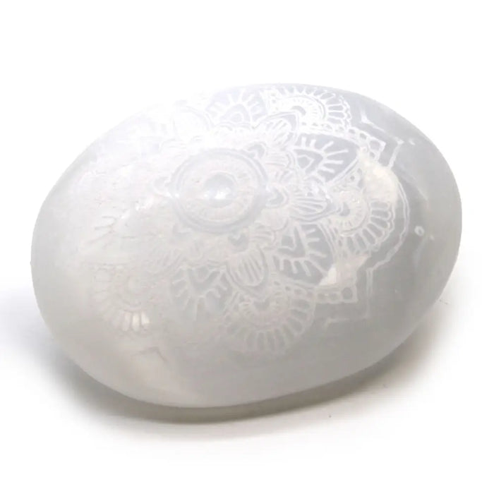 A translucent white selenite palm stone with an intricately engraved mandala design on its surface