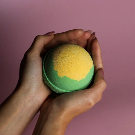 A vibrant green and yellow bath bomb with a textured surface held in hands from the apple pie bath bombs set