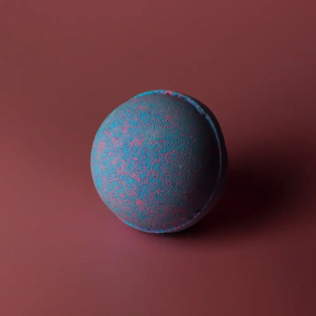 A spherical baby powder bath bomb with a textured surface and blue and pink speckles in a set of 3 bath bombs