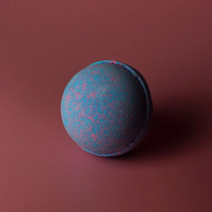 A spherical baby powder bath bomb with a textured surface and blue and pink speckles in a set of 3 bath bombs