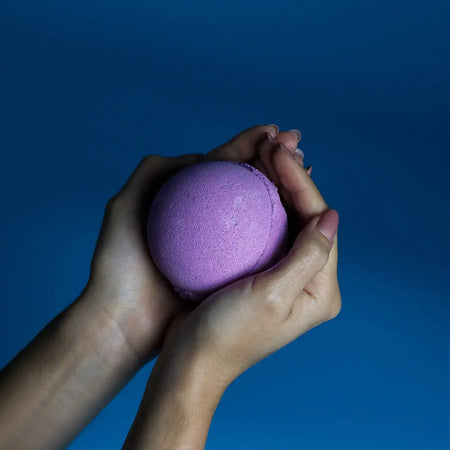 A soft purple spherical bath bomb held in two hands from a set of 3 bath bombs blackberry collection