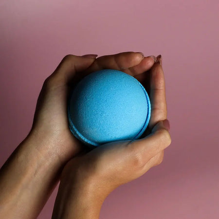 A vibrant blue round bath bomb with a textured surface held gently in hands from a set of 3 bath bombs blueberry