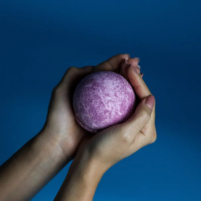 A round purple bath bomb with a glittery finish from a set of 3 cherry bath bombs