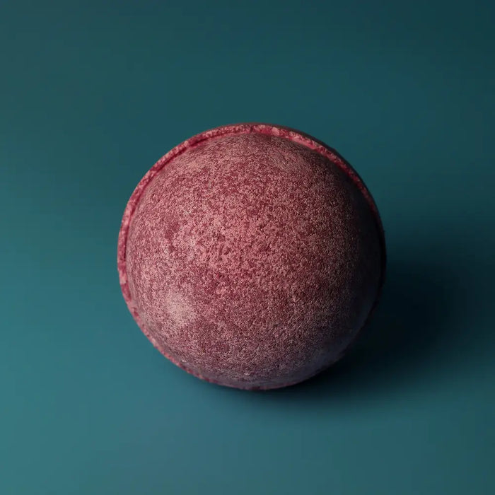 A round textured bath bomb with speckled pink and purple hues from a set of 3 bath bombs cherry edition