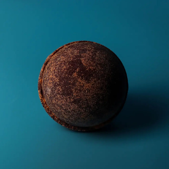 A round dark brown chocolate bath bomb with a textured speckled surface from a set of 3 bath bombs chocolate and orange