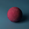 A round deep magenta bath bomb with a textured surface from a set of 3 bath bombs cranberry
