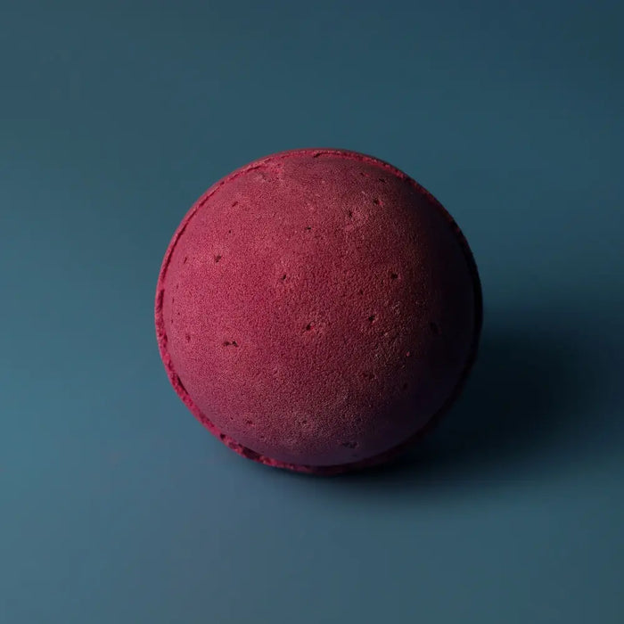 A round deep magenta bath bomb with a textured surface from a set of 3 bath bombs cranberry
