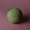 A round textured green bath bomb with orange speckles from a set of 3 bath bombs hawaiian mango scent