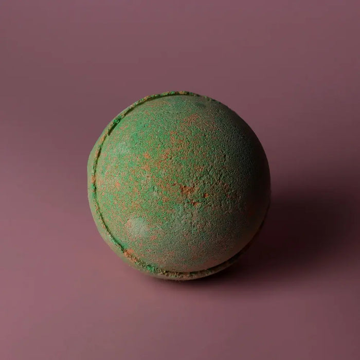 A round textured green bath bomb with orange speckles from a set of 3 bath bombs hawaiian mango scent
