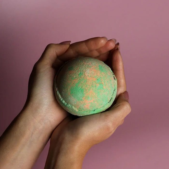 A round speckled green and orange bath bomb held in hands from the set of 3 bath bombs hawaiian mango